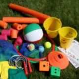 Large dice, buckets, pool noodles, jump rope, and balls, all displayed on the grass.